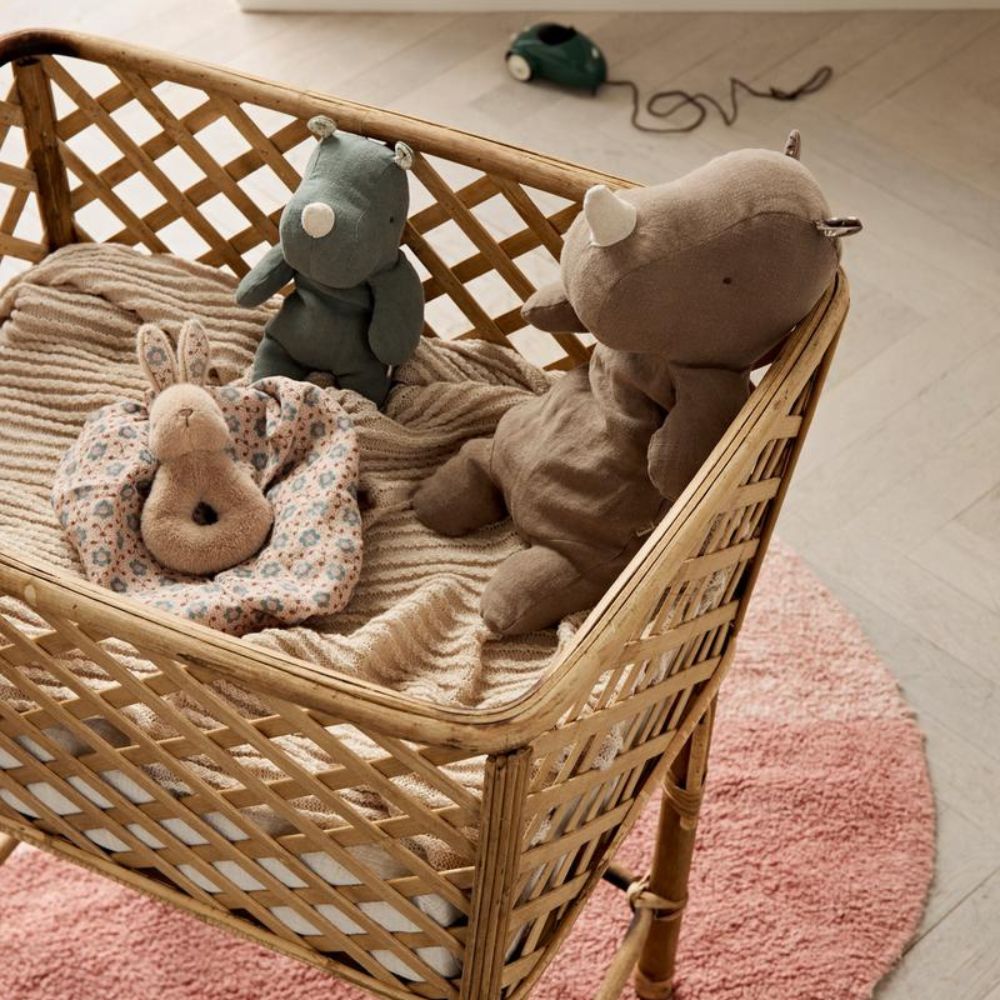 Soft Maileg baby toys including a rhino, bear, and bunny comforter placed in a wicker crib with a striped blanket