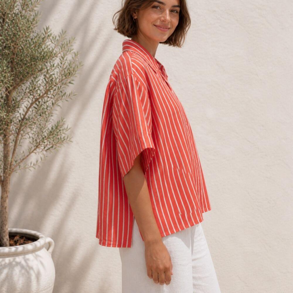 Woman wearing a red and white striped Marimekko shirt standing next to a potted plant against a beige wall.