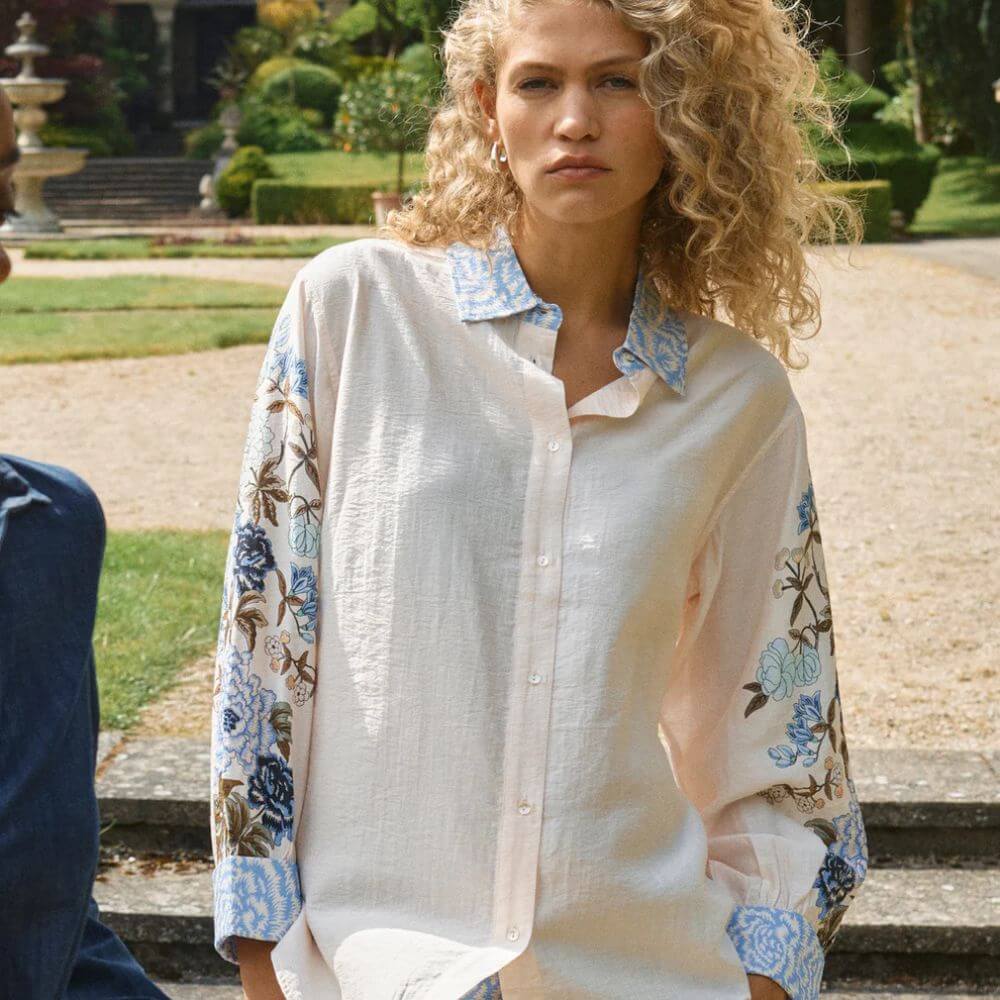 Woman wearing a light-colored shirt with floral sleeves in an outdoor setting