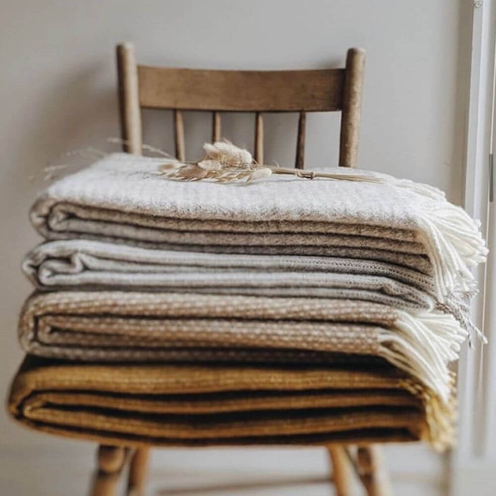 A folded pile of earthy coloured Klippan blankets on a wooden chair