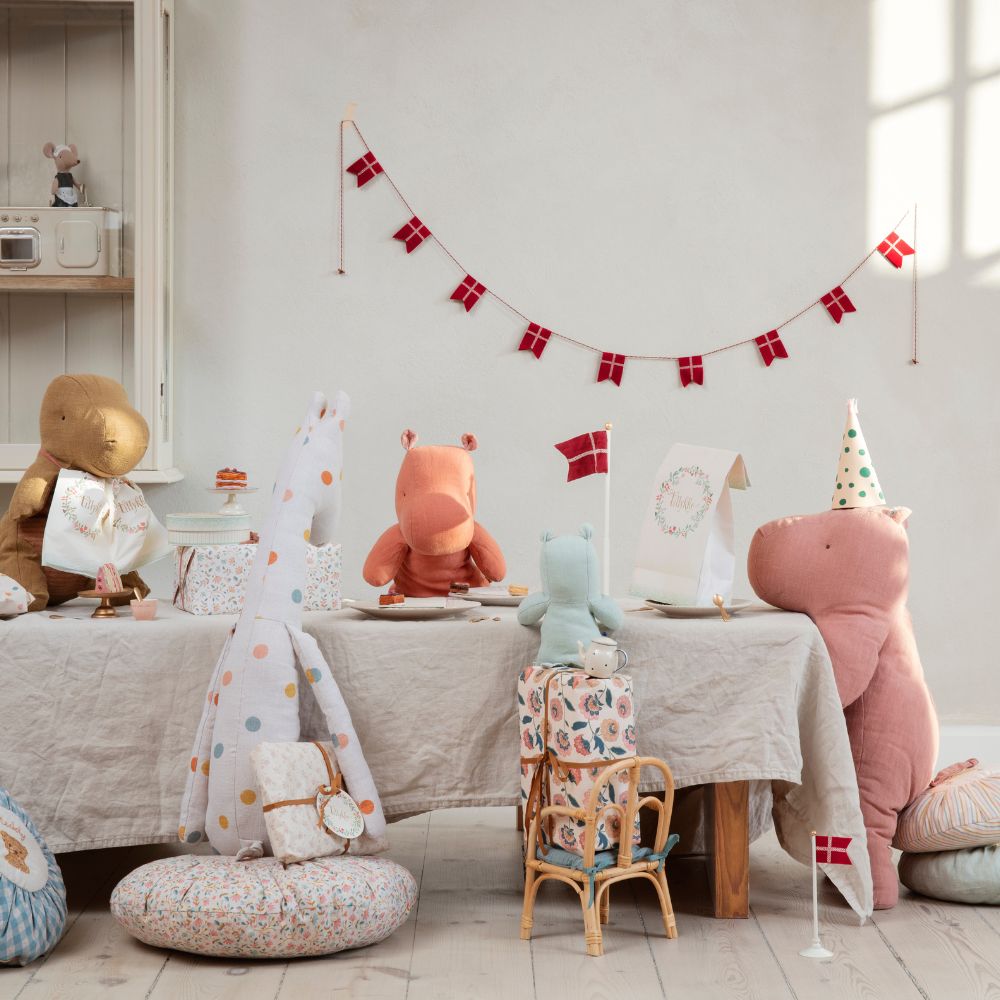 Maileg soft toys gathered around a decorated table for a pretend party, with miniature cakes, Danish flag bunting, and cosy room décor