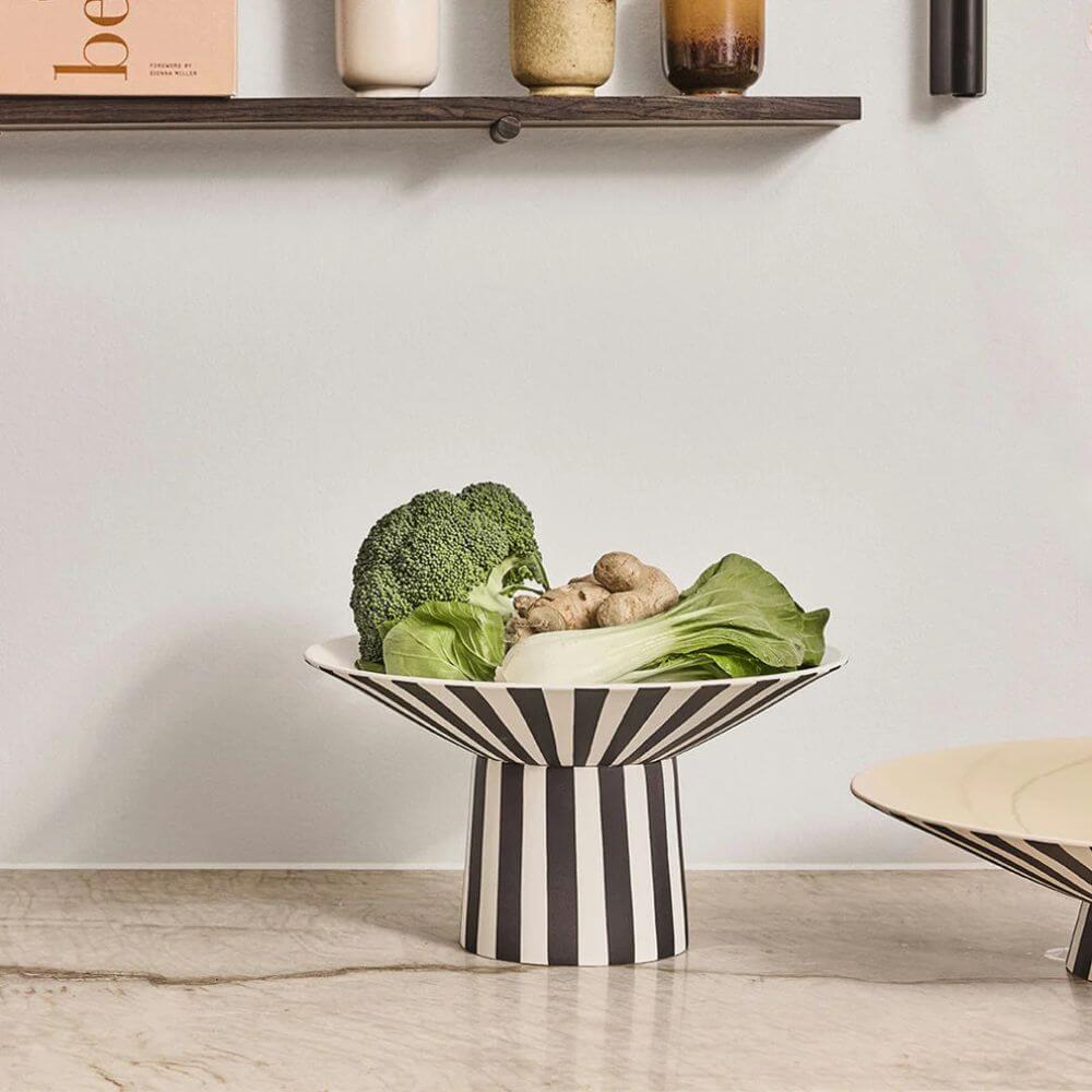 Striped bowl with vegetables on a light wooden floor against a white wall.