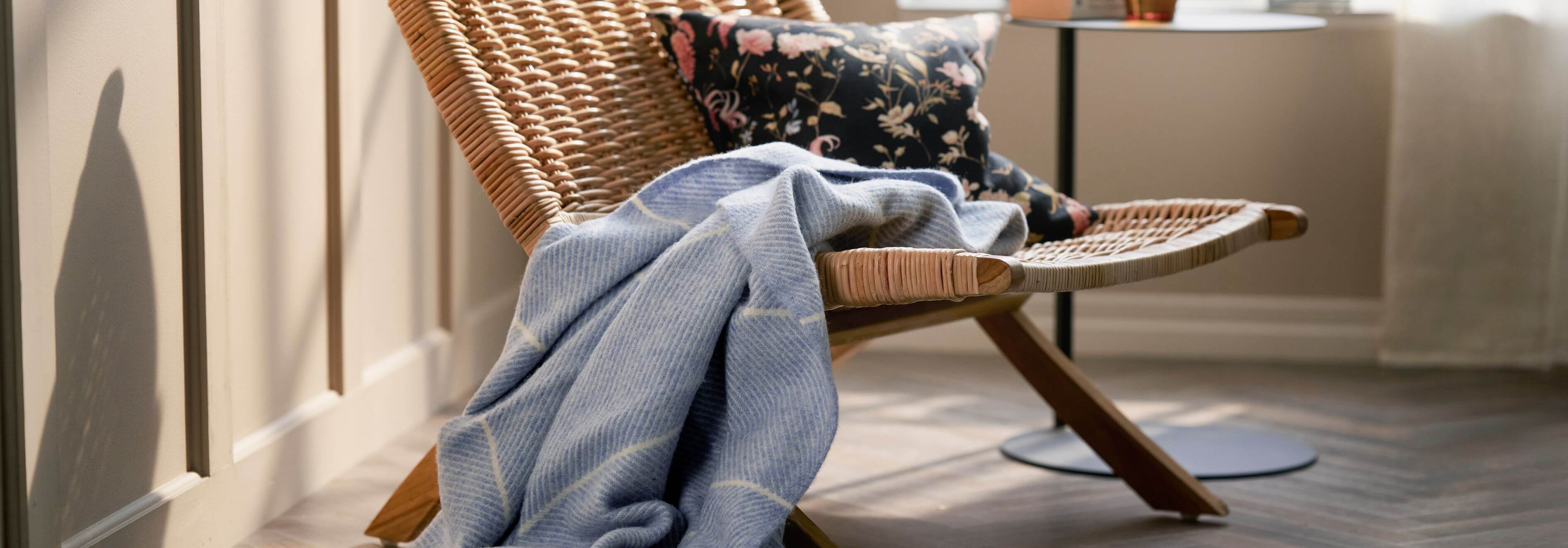 Wicker chair with a blue Klippan blanket draped over it in a room with light-coloured walls.