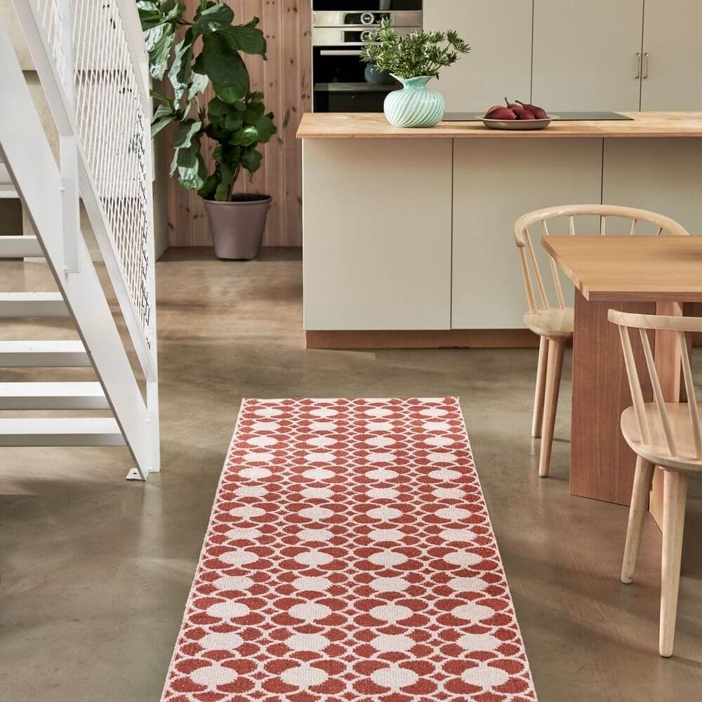 Red and white Pappelina rug on a concrete floor in a modern kitchen.