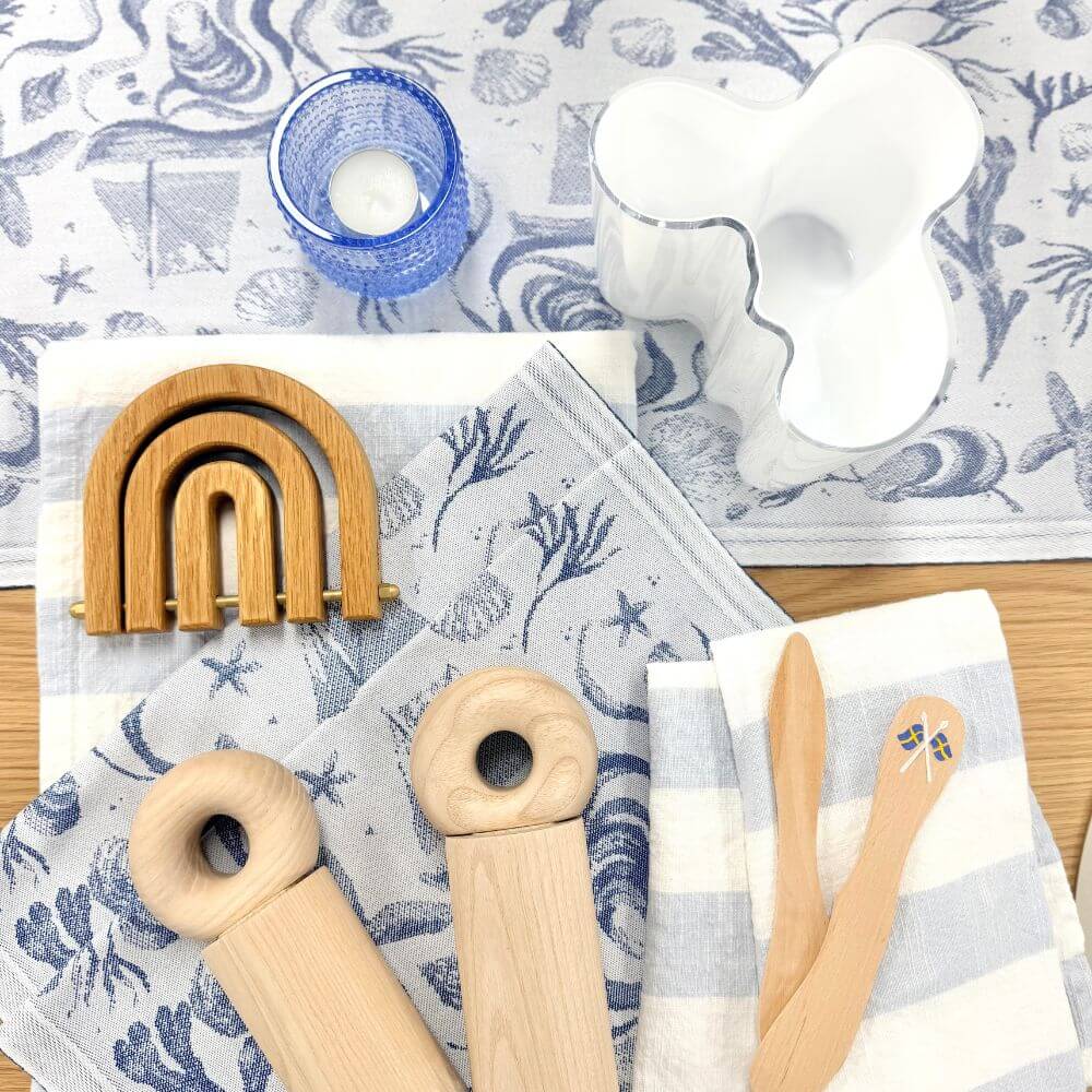 Ekelund Table Runners and Tea Towls laid on an oak table with an OYOY wooden trivet, OYOY Hoop Salt & Pepper grinders and Iitalla vases and andel holder